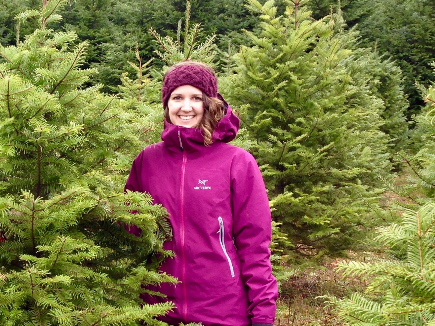 Kaitlyn is smiling at the camera while standing amongst short trees.